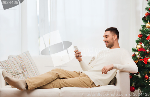 Image of smiling man with smartphone at home for christmas