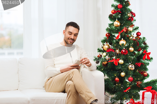 Image of smiling man with smartphone at home for christmas