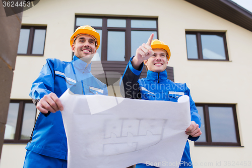 Image of smiling builders with blueprint pointing finger
