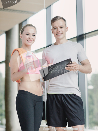 Image of smiling young woman with personal trainer in gym