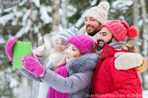 Image of smiling friends with tablet pc in winter forest