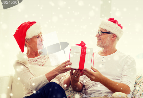 Image of happy senior couple in santa hats with gift box