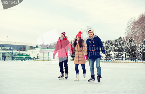 Image of happy friends ice skating on rink outdoors