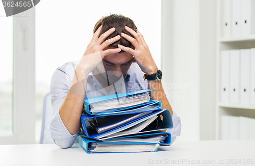 Image of sad businessman with stack of folders at office