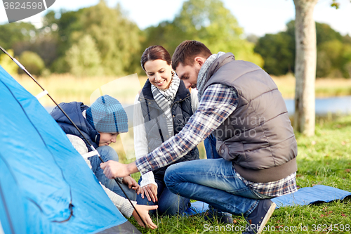 Image of happy parents and son setting up tent outdoors