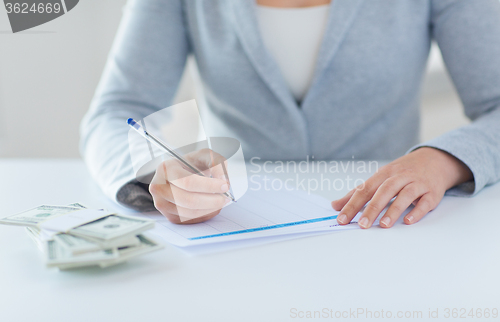 Image of close up of hands with money filling tax form