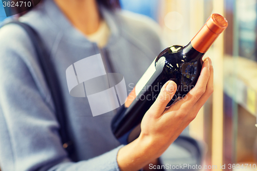 Image of happy woman choosing and buying wine in market