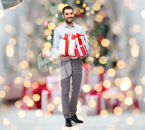 Image of happy man holding gift boxes over christmas lights