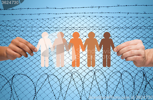 Image of hands holding people pictogram over barb wire