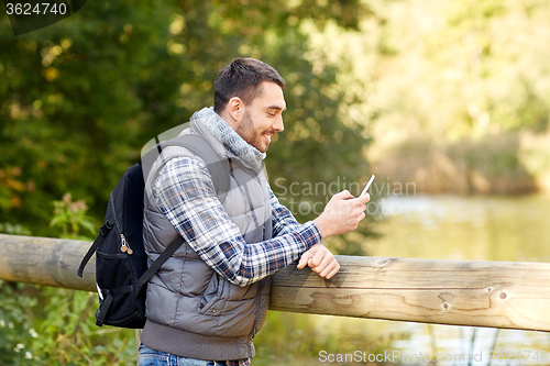 Image of happy man with backpack and smartphone outdoors