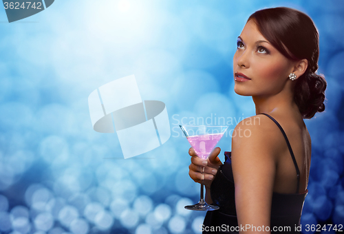 Image of smiling woman holding cocktail over blue lights