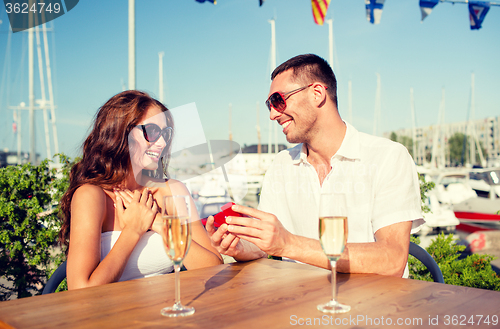 Image of smiling couple with champagne and gift at cafe