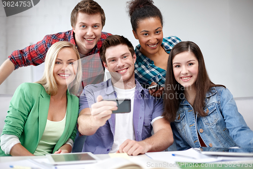 Image of group of happy students with smartphone at school