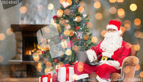 Image of santa claus with laptop in armchair at home