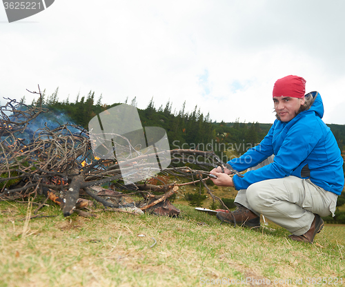 Image of hiking man prepare tasty sausages on campfire