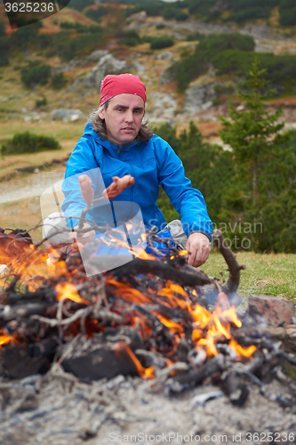 Image of hiking man prepare tasty sausages on campfire