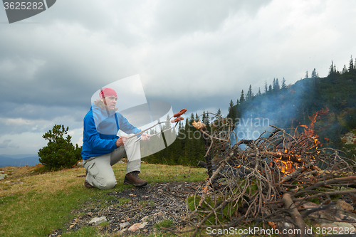 Image of hiking man prepare tasty sausages on campfire