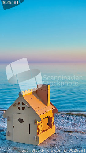 Image of Toy house made of corrugated cardboard in the sea coast at sunset.