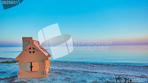 Image of Toy house made of corrugated cardboard in the sea coast at sunset.