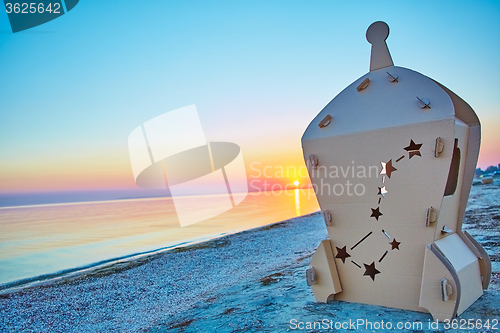 Image of Cardboard toy spaceship at sea coast and sunset.