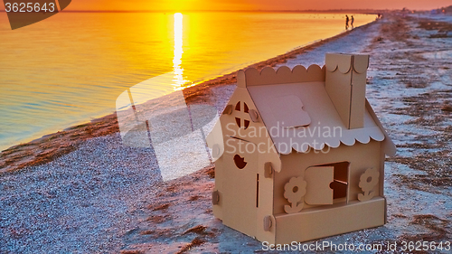 Image of Toy house made of corrugated cardboard in the sea coast at sunset.