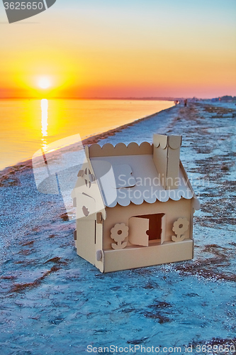 Image of Toy house made of corrugated cardboard in the sea coast at sunset.