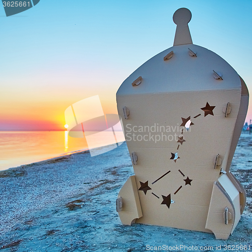 Image of Cardboard toy spaceship at sea coast and sunset.