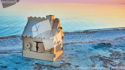 Image of Toy house made of corrugated cardboard in the sea coast at sunset.