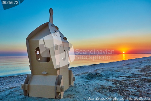 Image of Cardboard toy spaceship at sea coast and sunset.