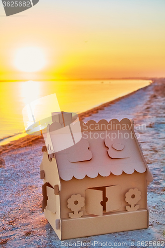 Image of Toy house made of corrugated cardboard in the sea coast at sunset.