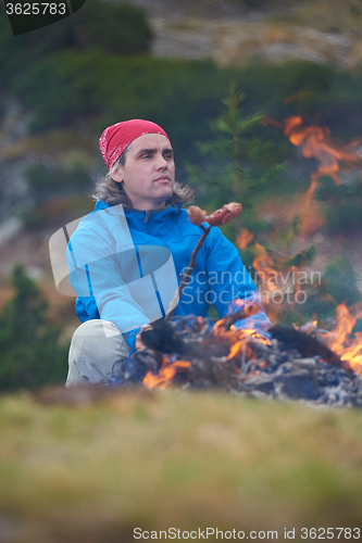 Image of hiking man prepare tasty sausages on campfire