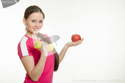 Image of Sportswoman holding a dumbbell in your right hand and an apple in his left hand