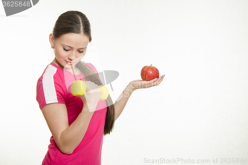Image of Athlete shakes muscles of his right hand holding an apple and a dumbbell in your left hand