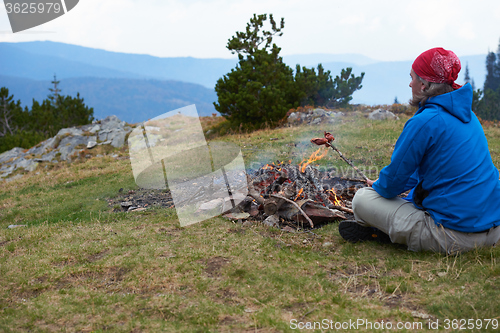 Image of hiking man prepare tasty sausages on campfire