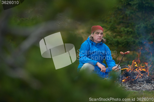 Image of hiking man prepare tasty sausages on campfire