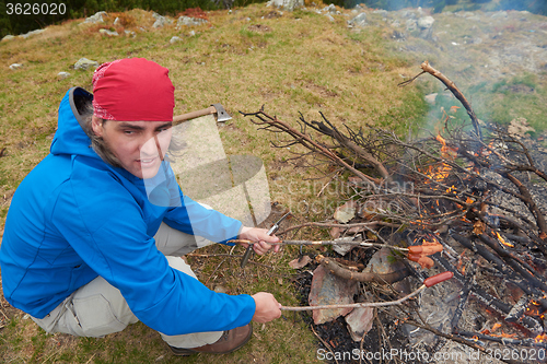 Image of hiking man prepare tasty sausages on campfire