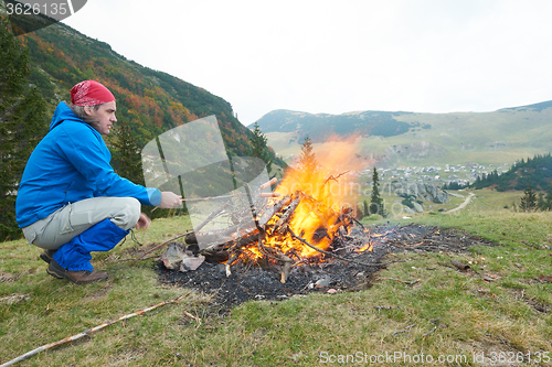 Image of hiking man prepare tasty sausages on campfire