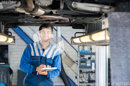 Image of Happy Mechanic Writing On Clipboard Under Car