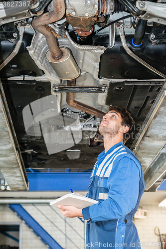 Image of Mechanic With Clipboard Examining Under Car In Garage