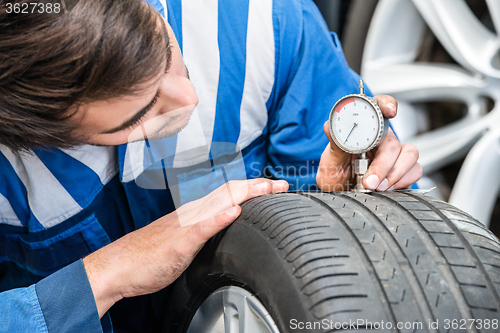 Image of Mechanic Pressing Gauge Into Tire In Garage