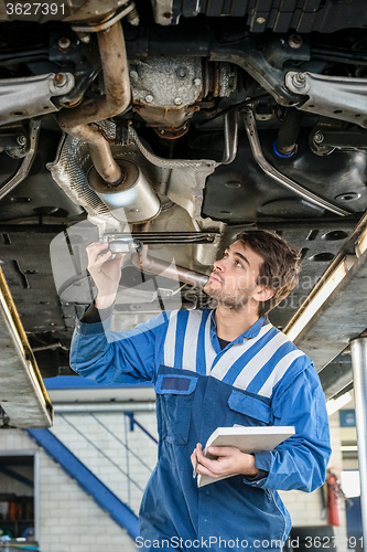 Image of Mechanic Examining Exhaust System Of Car With Flashlight