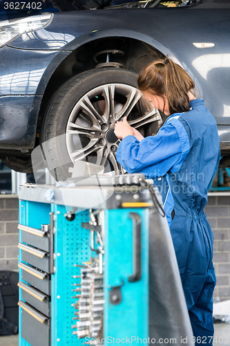 Image of Mechanic Changing Tire From Suspended Car In Garage