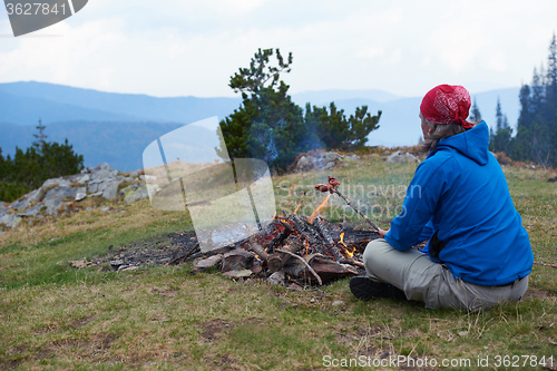 Image of hiking man prepare tasty sausages on campfire