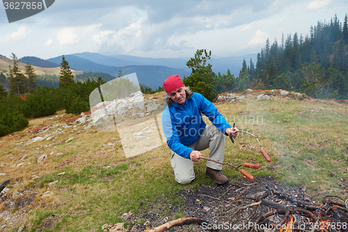 Image of hiking man prepare tasty sausages on campfire