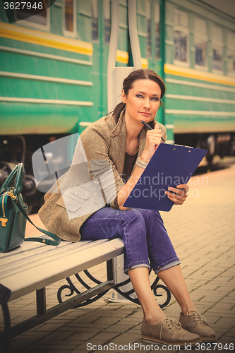 Image of beautiful middle-aged woman-traveler sitting on a bench, holding