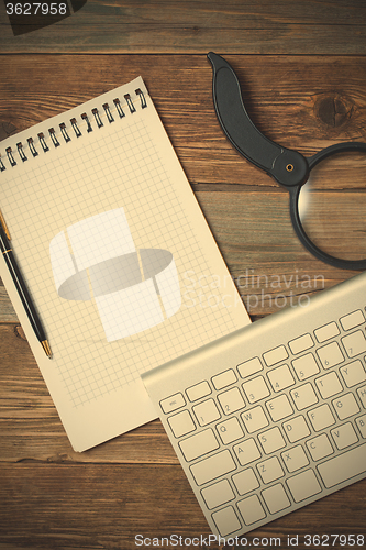 Image of Computer keyboard, notebook, pen and magnifying glass