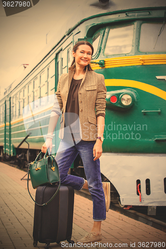 Image of smiling middle-aged woman with luggage near old train