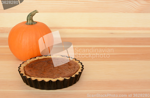 Image of Mini pumpkin pie with orange pumpkin on wood