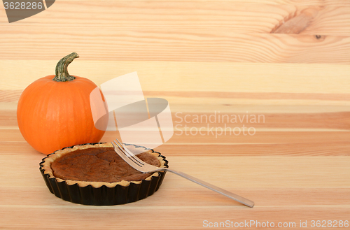 Image of Fork with a small pumpkin pie on wood