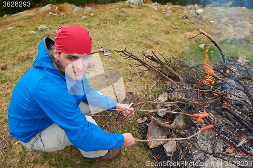 Image of hiking man prepare tasty sausages on campfire